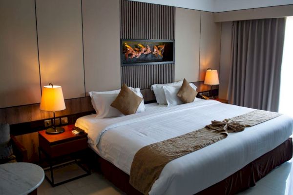 This image shows a neatly arranged hotel room with a king-size bed, wall-mounted lamps on nightstands, and a small table by a window with curtains.