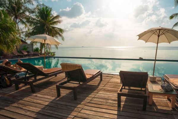 A tranquil poolside scene with several lounge chairs and umbrellas, overlooking a serene ocean view under a partly cloudy sky.