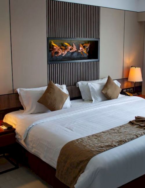 A modern hotel room with a large bed, two bedside tables with lamps, decorative pillows, wall art, and a window with closed curtains.