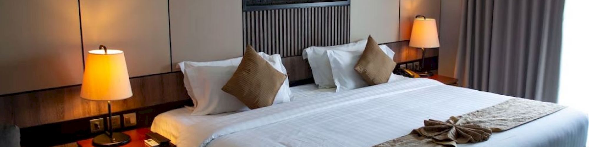 A neatly arranged hotel room with a large bed, bedside tables with lamps, and a decorative piece on the wall above the bed, ending the sentence.