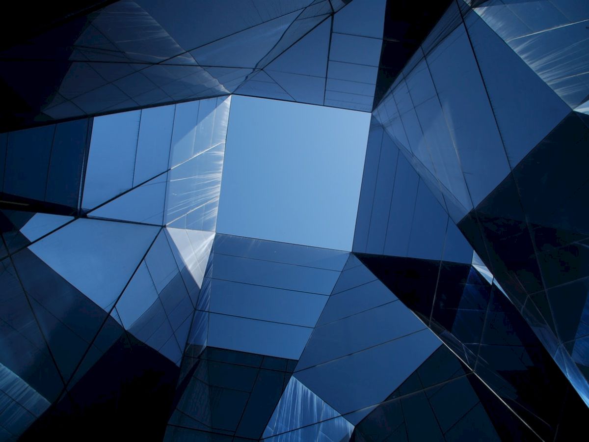 The image shows a futuristic architectural design with reflective glass surfaces creating a geometric pattern, opening to a blue sky.