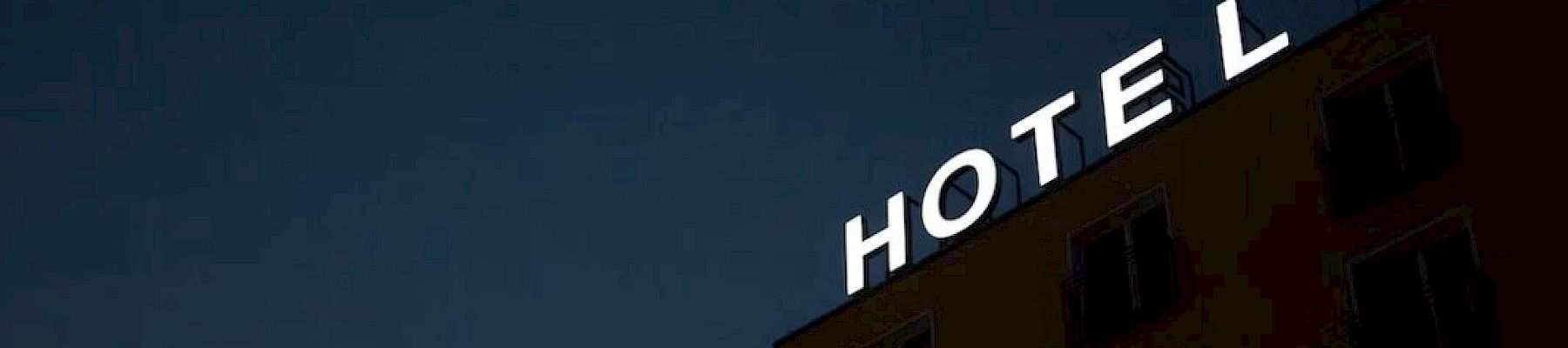 A building with a lit sign reading "HOTEL" against a dark sky background. The top part of the building and windows are slightly visible.