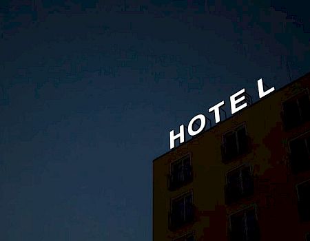 A building with a lit sign reading "HOTEL" against a dark sky background. The top part of the building and windows are slightly visible.