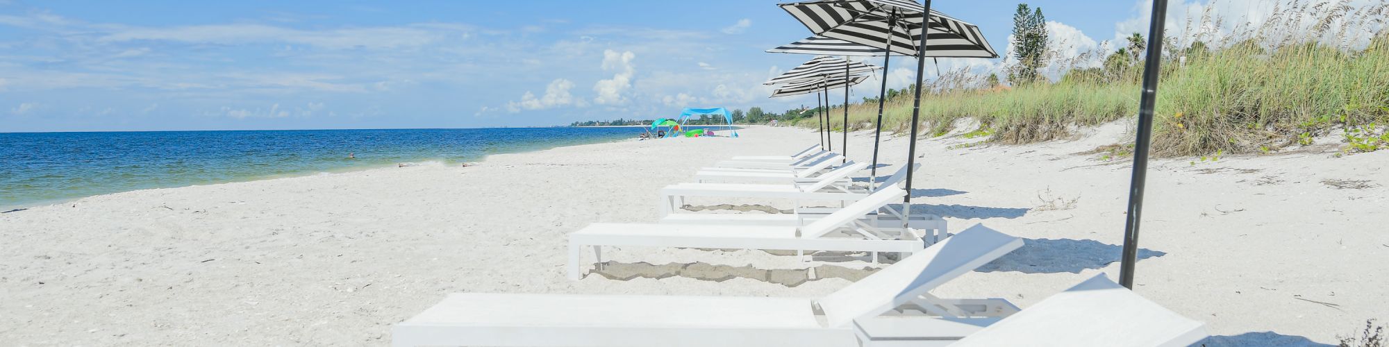 This image shows a beautiful beach with white sandy shores, lined with white lounge chairs and striped umbrellas under a clear blue sky.