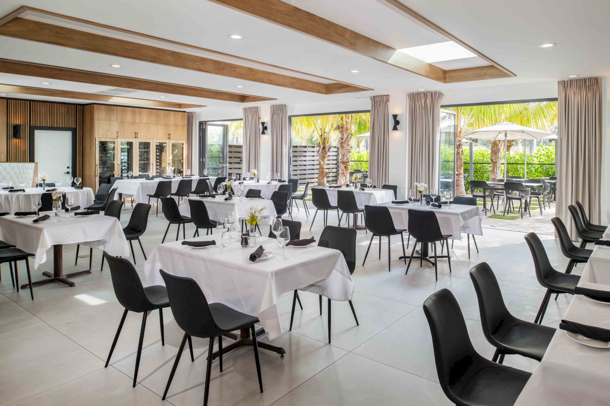 This image shows a modern, spacious dining area with neatly arranged tables and chairs, bright lighting, and large windows offering a view outside.