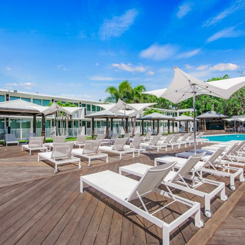 This image shows a resort scene with numerous white lounge chairs and umbrellas on a wooden deck, surrounding an outdoor pool. The sentence ends.