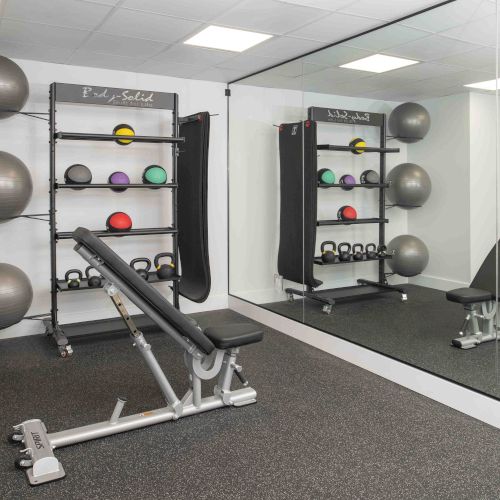 This image shows a small workout room with exercise balls, kettlebells, a bench, and a large mirror. The equipment is organized on shelves.