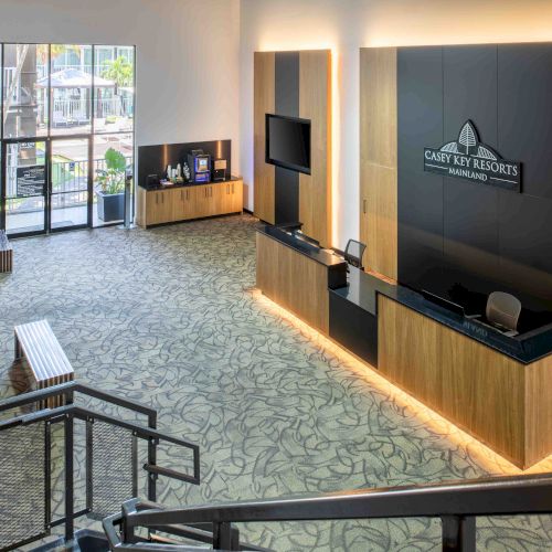 The image shows a modern hotel lobby with a reception desk, seating area, and large windows letting in natural light.