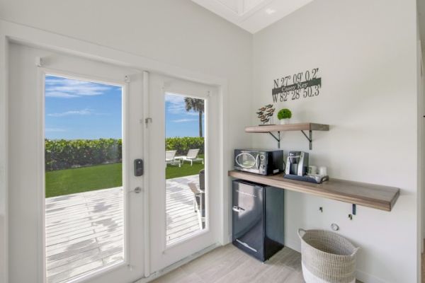 A bright room with French doors opens to a scenic outdoor view. Inside, it has a mini-fridge, microwave, coffee maker, and wall shelves for storage.