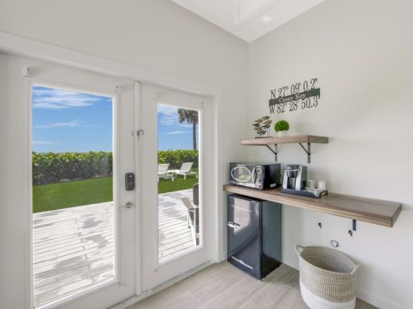 A bright room with French doors opens to a scenic outdoor view. Inside, it has a mini-fridge, microwave, coffee maker, and wall shelves for storage.