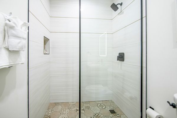 A modern bathroom with a glass-enclosed shower, white tiles, a wall-mounted showerhead, and a towel rack on the left wall, ending the sentence.