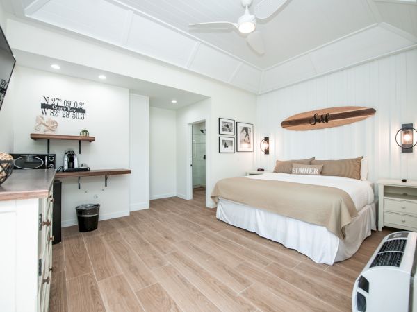 A cozy bedroom with a king-size bed, minimalistic decor, wall art, wood flooring, a ceiling fan, and a small coffee nook in the corner ending the sentence.