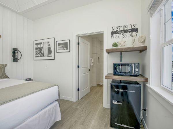 A cozy room with a bed, framed pictures, a mini-fridge, microwave, a window with a view, and an open door leading to a bathroom.