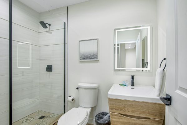 A modern bathroom with a glass shower, a toilet, a wooden vanity with a sink, a mirror, a towel rack, and minimalistic decor.