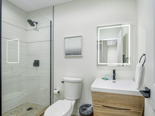 A modern bathroom with a glass shower, a toilet, a wooden vanity with a sink, a mirror, a towel rack, and minimalistic decor.