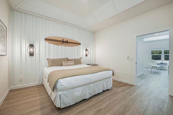 A cozy bedroom featuring a large bed with beige bedding, wall decor with a wooden surfboard, and two wall lamps.