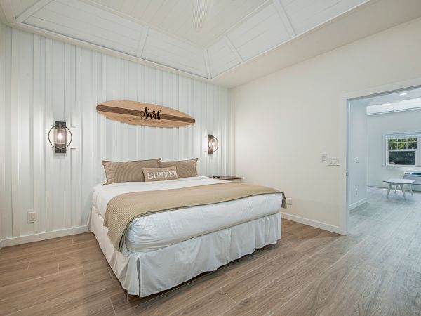 A cozy bedroom featuring a large bed with beige bedding, wall decor with a wooden surfboard, and two wall lamps.
