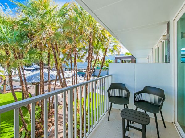 A cozy balcony with two chairs and a small table, overlooking a garden full of palm trees on a sunny day.