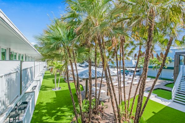 The image showcases a well-maintained outdoor area with palm trees, green lawns, and white buildings. The sky is clear and blue.