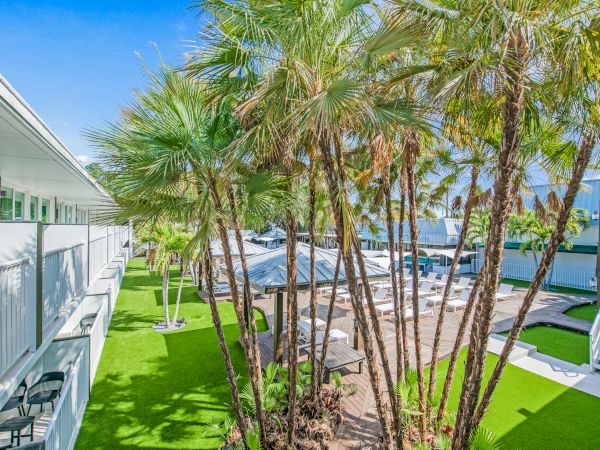 The image showcases a well-maintained outdoor area with palm trees, green lawns, and white buildings. The sky is clear and blue.