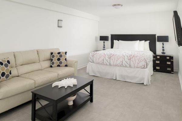 A modern, minimalist bedroom with a king-sized bed, beige sofa, two nightstands with lamps, and a black coffee table with decor items on it.