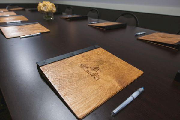 A conference room table set with wooden notepads, pens, and a flower arrangement in the center, ready for a meeting.