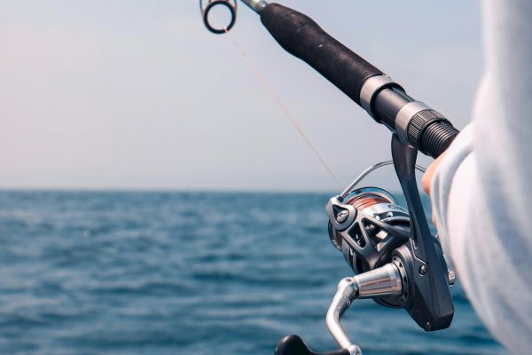 A person is holding a fishing rod over a body of water, ready to fish on a clear day, with the ocean in the background.