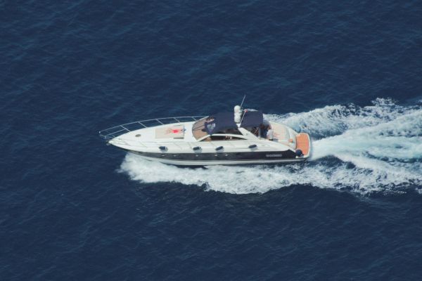 A white motorboat with two people aboard speeds across the ocean, creating a wake behind it, against a backdrop of deep blue water.