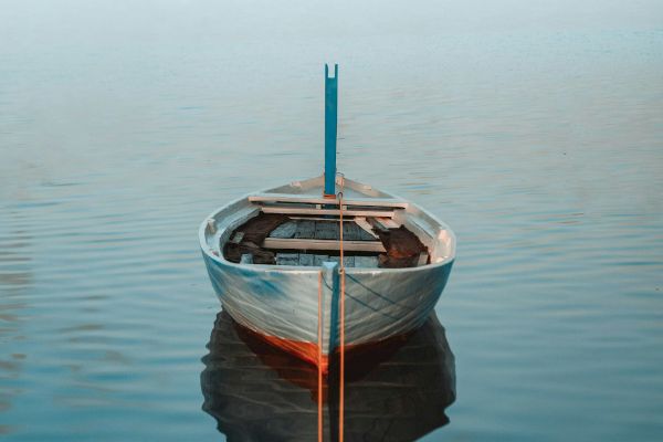 A lone rowboat is anchored on calm water, creating a serene and tranquil scene with its reflection mirrored perfectly.