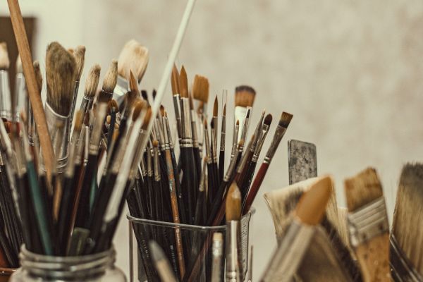 The image shows various art paintbrushes and other painting tools organized in jars on a table, likely in an artist's studio.