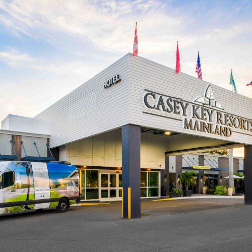 The image shows the entrance of Casey Key Resorts Mainland with a van parked in front. The building has flags on top and palm trees nearby.