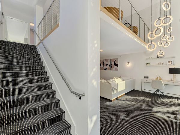 This image shows a modern interior with a staircase, sofa, desk, and unique hanging lights in a bright space.