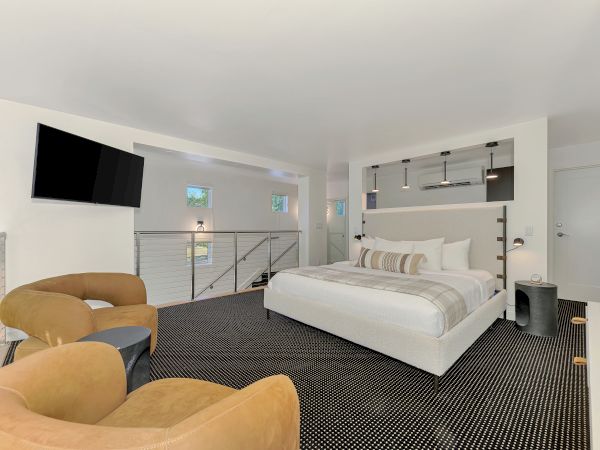 A modern bedroom with a large bed, chic chairs, and wall-mounted TV in a bright, minimalist style.