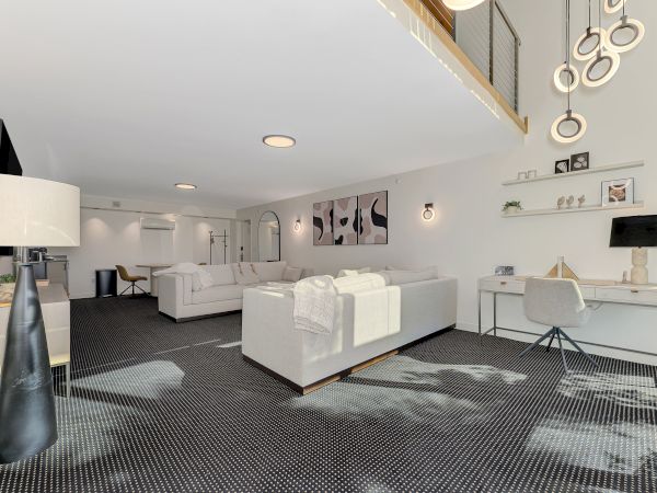 A modern living room with a white sofa, desk, and artistic decor, featuring a high ceiling and contemporary lighting design.