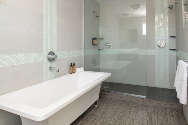 A modern bathroom with a freestanding bathtub, a spacious glass-enclosed shower, wall-mounted toiletries, and a towel hanging on the right.