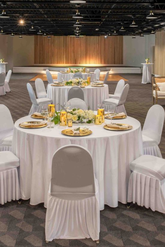 The image shows an event hall with round tables covered in white cloth, set for a banquet, and decorated with flowers and candles, ending the sentence.