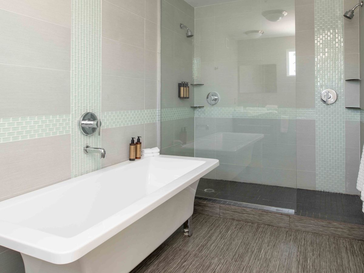 A modern bathroom features a free-standing bathtub, glass-enclosed shower, striped tiling, and minimalist decor, including mounted toiletries and a towel rack.