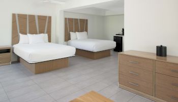 A hotel room with two double beds, a dresser, a side table, and a coffee maker placed on a surface near the corner.