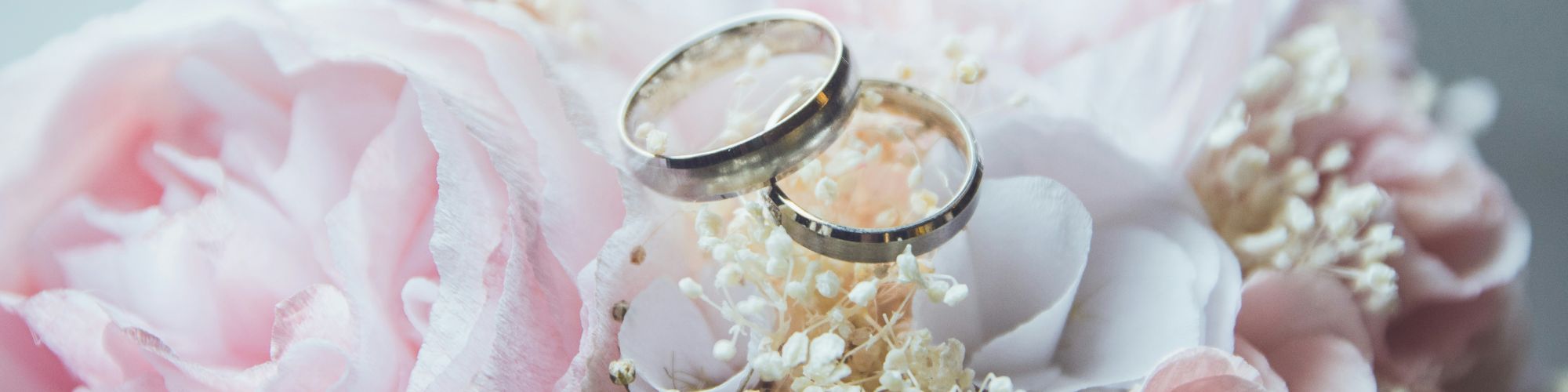 Two wedding rings rest on a bouquet of pastel-colored flowers, including roses and small blossoms.