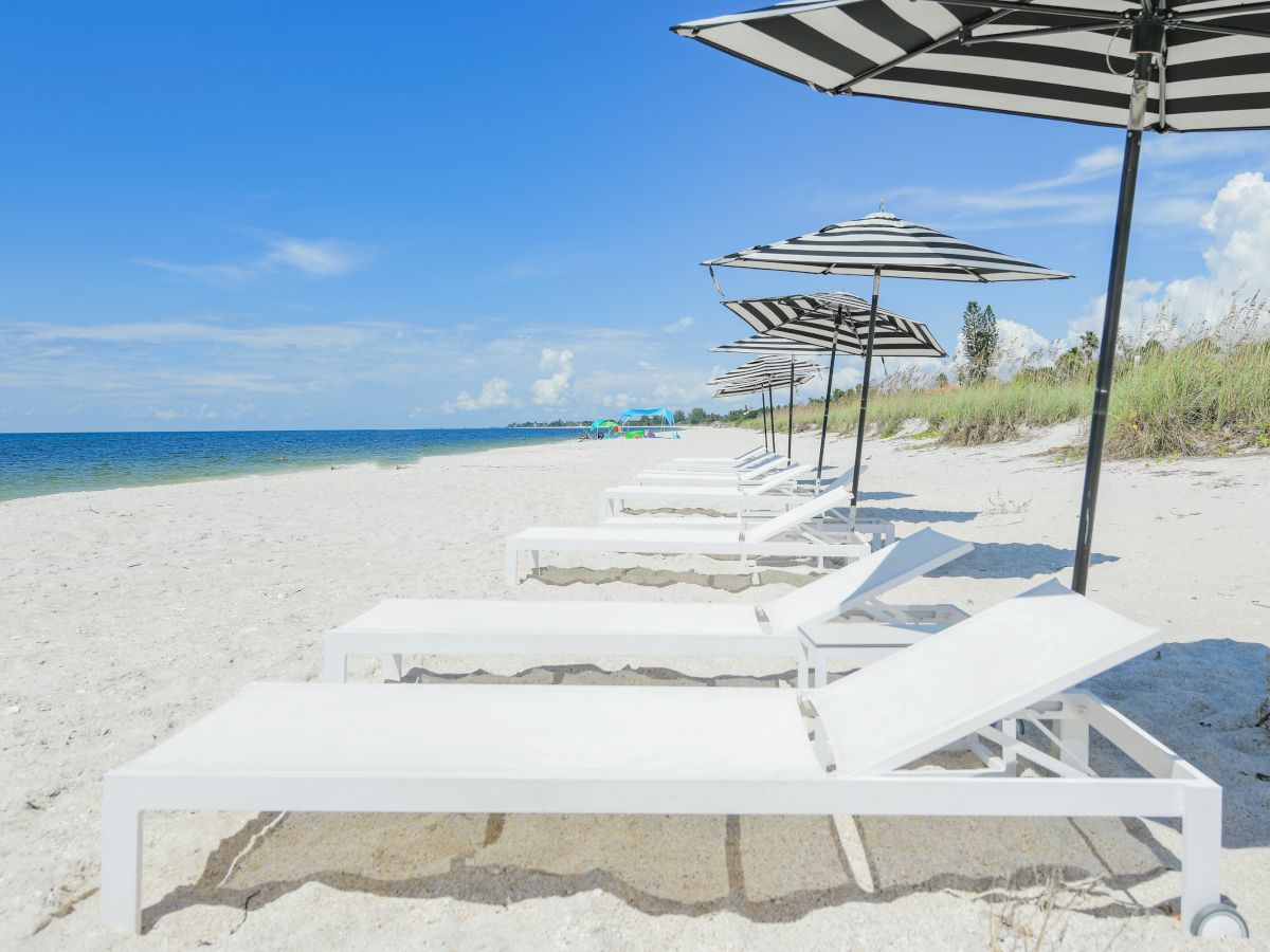 A serene beach scene featuring white lounge chairs and striped umbrellas lined up on the sandy shore under a clear blue sky.