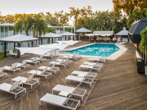 A serene poolside area with lounge chairs, umbrellas, and wooden decking, surrounded by lush greenery and modern buildings.
