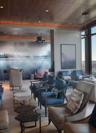 A modern lounge with plush seating, large windows showcasing a waterfront view, and a mural on the back wall, creating a comfortable atmosphere.