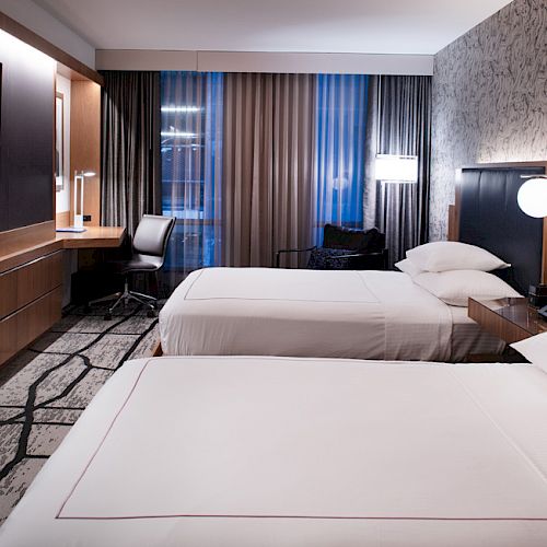 A modern hotel room with two beds, a work desk, a TV on the wall, contemporary lighting, and patterned wallpaper behind the beds ending the sentence.